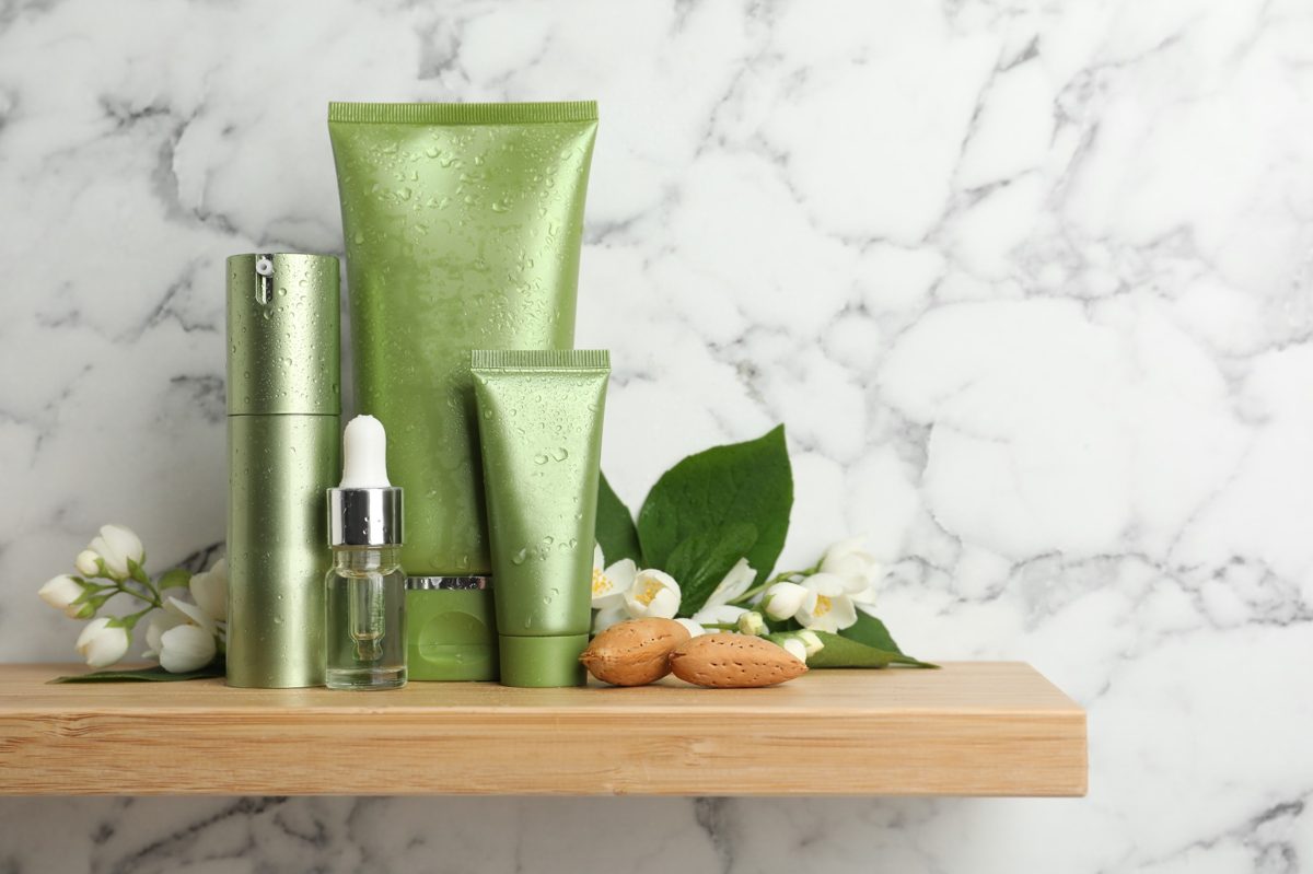 Natural green skincare products on a wooden shelf with flowers and almonds
